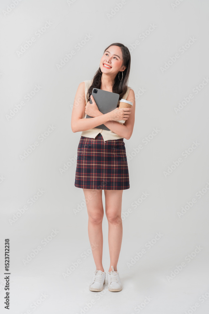 Young happy Asian female IT student wearing casual clothes and a backpack, holding a closed laptop computer while smiling confidently against a plain background. Celebrating success, learning Young happy Asian female IT student wearing casual clothes and a backpack, holding a closed laptop computer while smiling confidently against a plain background. Celebrating success, learning