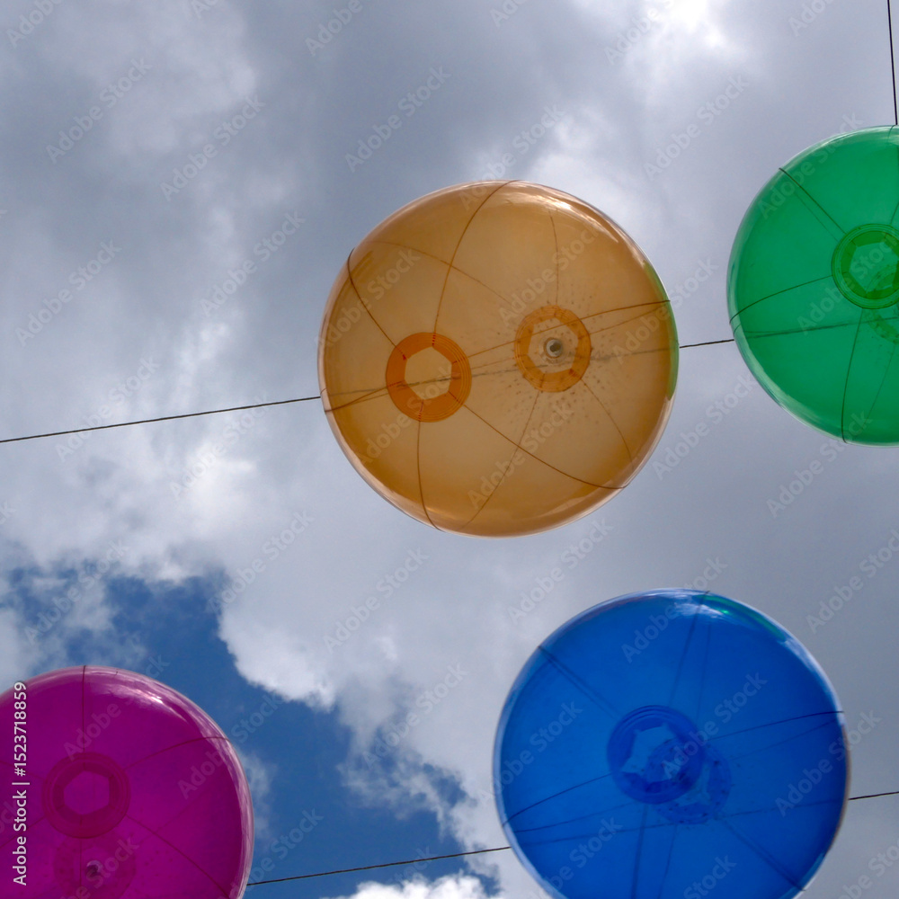 Fototapeta premium colorful balloons hanging in the sky in front of bright summer rain clouds