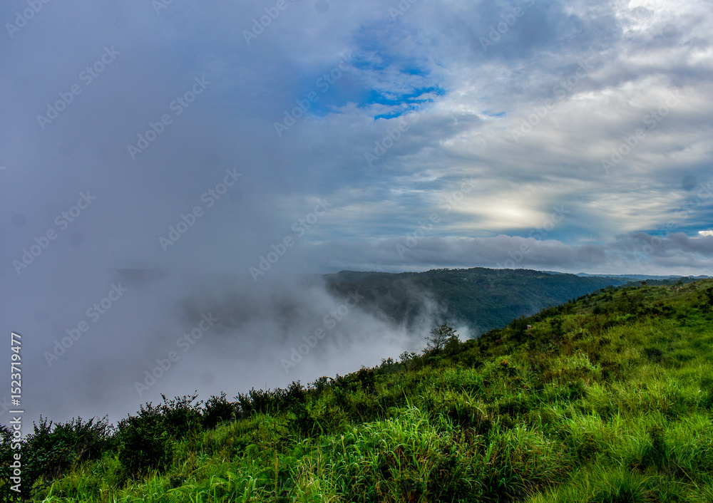 Fog envelops green hills and valleys, with clouds and blue sky overhead in Meghalaya. Fog envelops green hills and valleys, with clouds and blue sky overhead in Meghalaya.