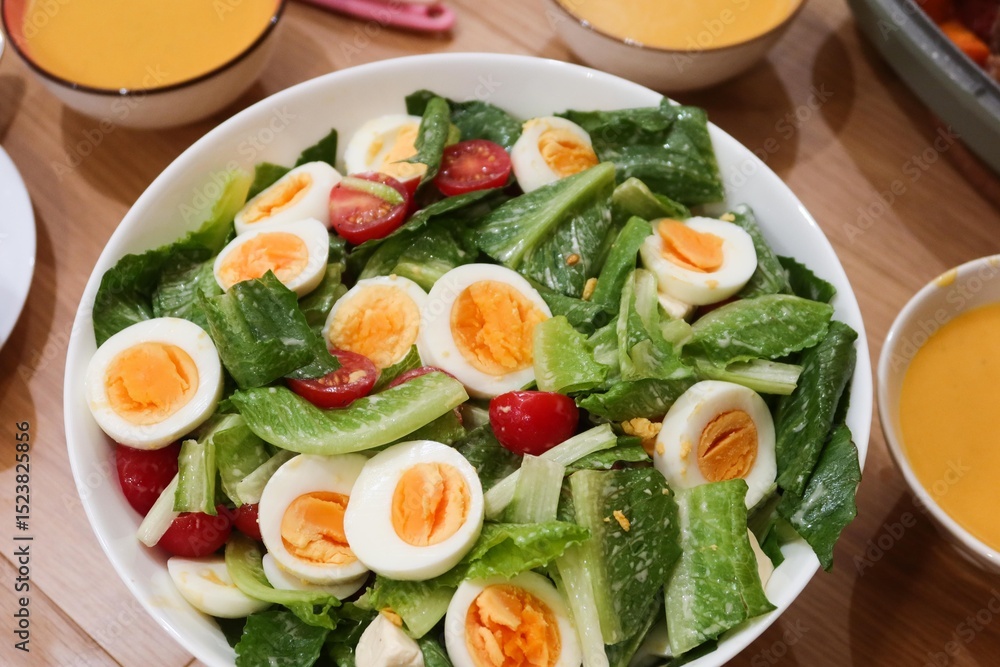 close up of homemade salad of boiled egg cut in slices, cherry tomato, lettuce in a big white bowl with pumpkin cream soup in the side close up of homemade salad of boiled egg cut in slices, cherry tomato, lettuce in a big white bowl with pumpkin cream soup in the side