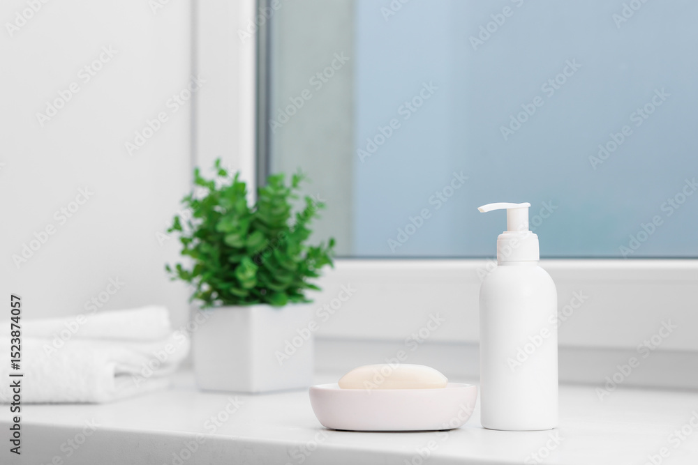 Fototapeta premium Soap bar, bottle of cosmetic product, towels and floral decor on white window sill indoors