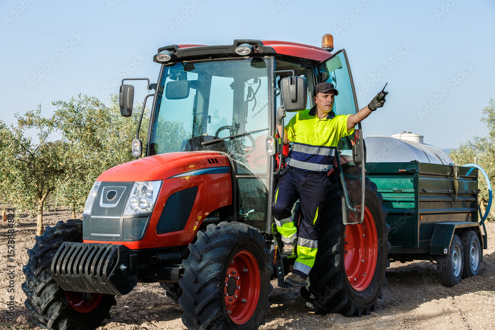 Obraz premium Farmer on a tractor points with his hand in an olive grove in Andalusia