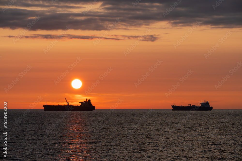 Silhouettes of two oil tankers against an orange sunset in the Baltic Sea. Maritime oil transportation, Estonia. Silhouettes of two oil tankers against an orange sunset in the Baltic Sea. Maritime oil transportation, Estonia.