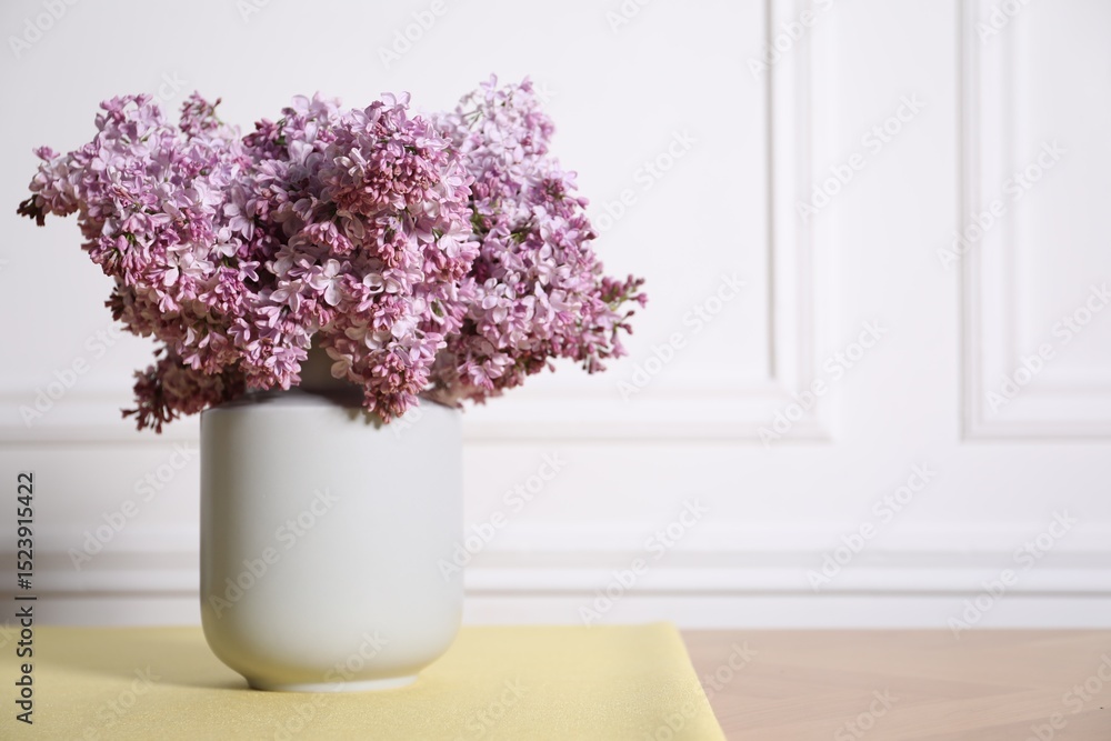 Fototapeta premium Beautiful lilac flowers in vase on table near white wall indoors, space for text