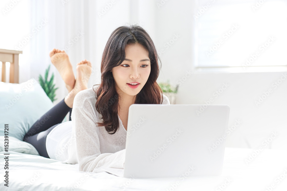 Thoughtful Young Asian Woman Working Remotely on Laptop in Bright Minimalist Home Office Thoughtful Young Asian Woman Working Remotely on Laptop in Bright Minimalist Home Office