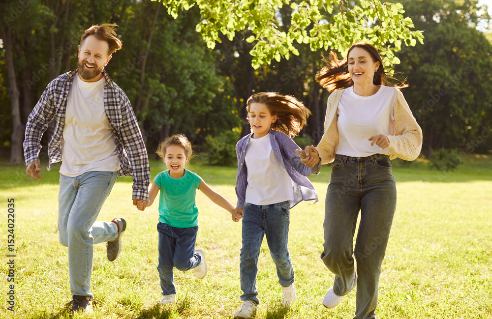 Fototapeta premium Happy family running and having fun in summer park enjoying sunny day in nature. Mother, father and two cheerful children boy and girl walking on green grass outdoors at sunset together.