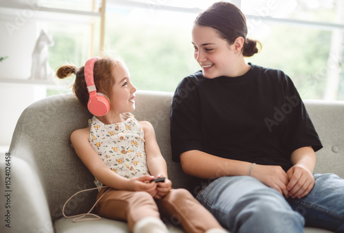 Fotografie babysitter teen sit on sofa listening music with cute 5 years child girl