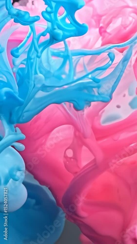 Bright blue and pink ink drops disperse and swirl together in clear liquid medium creating mesmerizing fluid dynamics with vibrant color mixing and organic flowing movements