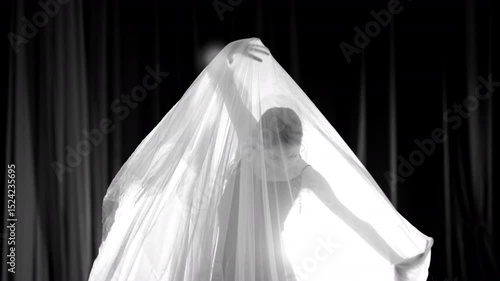 Young dancer performing with white veil on dark stage. Selective focus