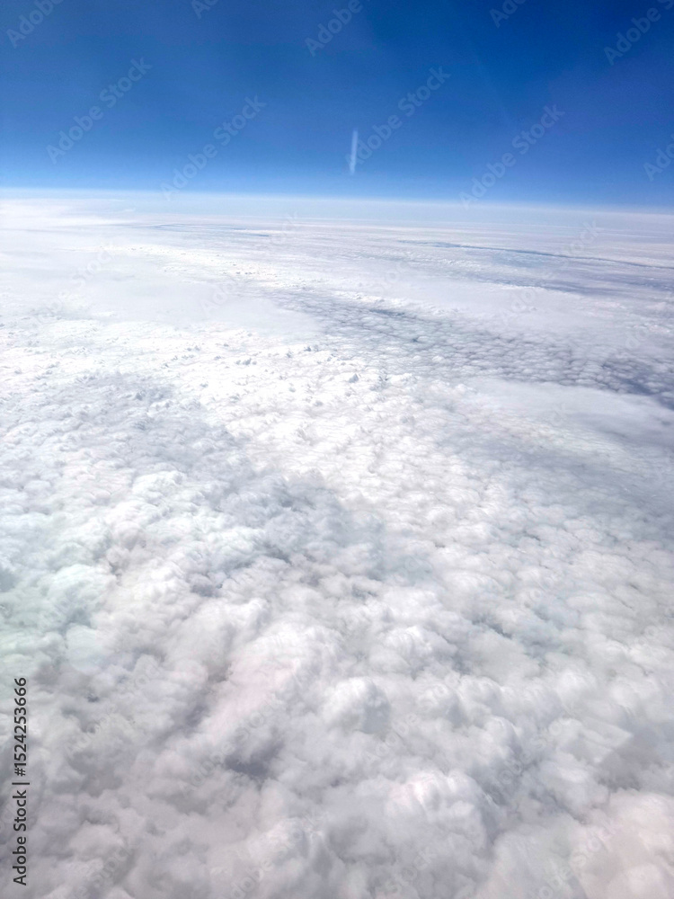 Naklejka premium A scenic view from the airplane window showing soft white clouds and the earth far below. The altitude offers a breathtaking perspective of the landscape and sky