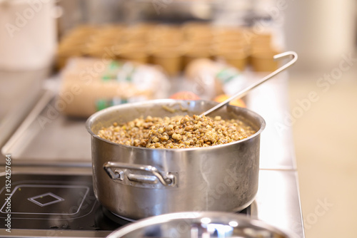 Large stainless steel pot filled with cooked lentils and pasta on a professional kitchen stove. Close-up of healthy meal preparation in a commercial food setting.