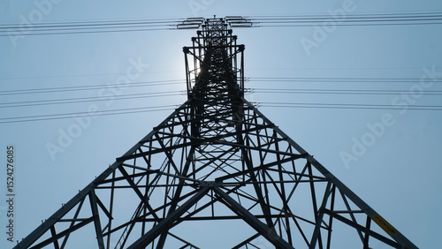 A towering electricity pylon against a clear blue sky, showcasing the structure's intricate metal framework and overhead power lines.