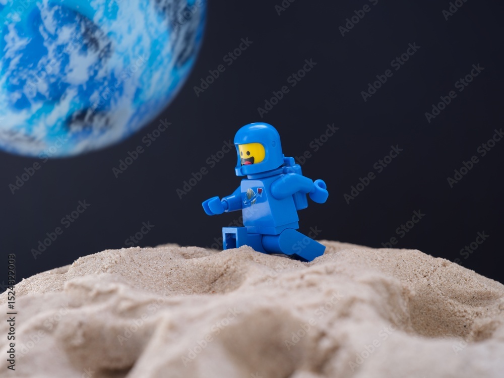 Obraz premium Tambov, Russian Federation - July 28, 2024 Blue Lego astronaut minifigure walking on sand on a planet against black space background with another blue planet in it
