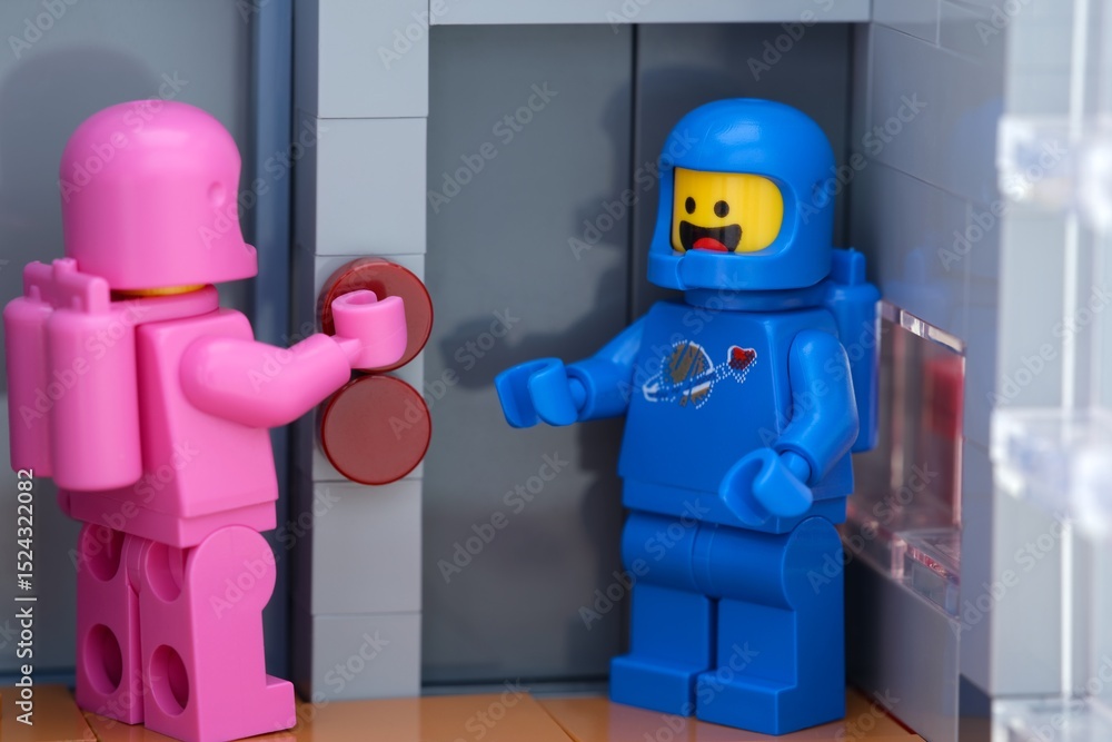 Obraz premium Tambov, Russian Federation - May 26, 2025 Two Lego astronaut minifigures waiting at an elevator. The pink one is pressing a button on the elevator. Close-up