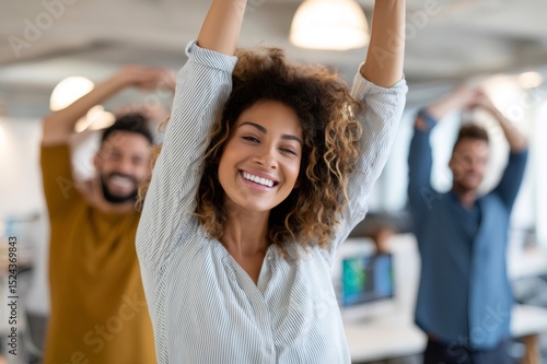 Smiling businesswoman stretching with arms raised in office with coworkers