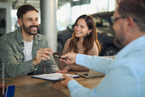 Happy couple about to sign a contract on a meeting with car salesperson in a showroom. 