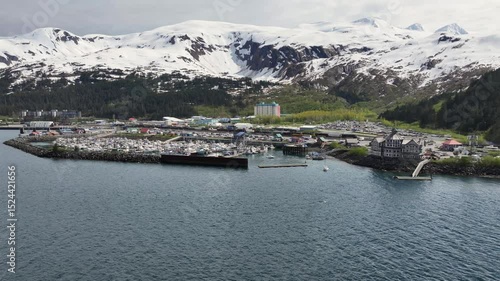 flying along Alaska mountain Landscape in front of Whittier harbor and port area with Cityscape of Whittier and snow covered mountains in background. 4k aerial video footage