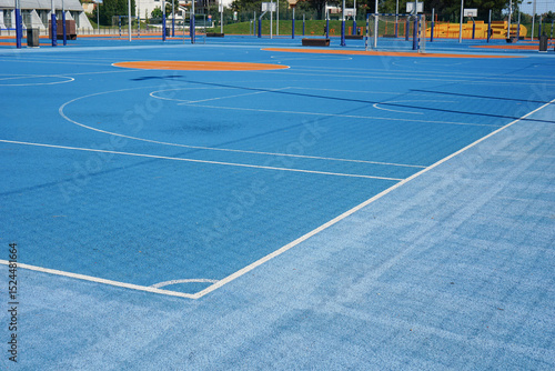 A new modern blue sports ground with a rubberized surface for safe athletic activities, featuring basketball courts and orange markings under a clear sky concept of urban recreation