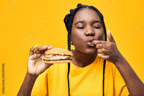 Photography Young woman enjoying a delicious hamburger with a playful expression, vibrant ye