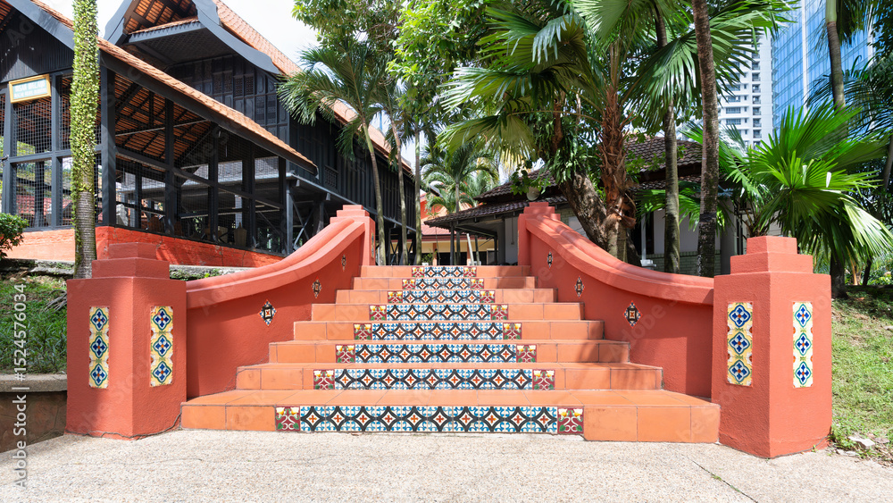 Fototapeta premium Colorful tiled stairs invite visitors to Muzium Negara, showcasing traditional Malaysian architecture. Palm trees and greenery enhance the serene atmosphere, making it a perfect spot for exploration