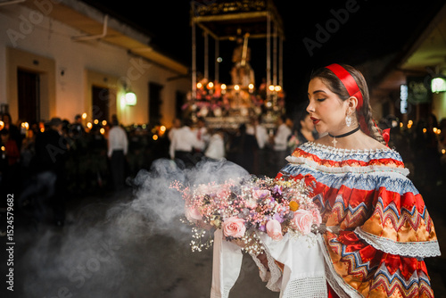 Mujer sahumadora vestida con traje típico tradicional participa en una procesión nocturna durante la Semana Santa en Popayán, Colombia. Sostiene un ramo de flores mientras esparce sahumerio 