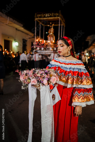 Mujer sahumadora vestida con traje típico tradicional participa en una procesión nocturna durante la Semana Santa en Popayán, Colombia. Sostiene un ramo de flores mientras esparce sahumerio 