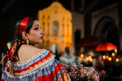 Mujer sahumadora vestida con traje típico tradicional participa en una procesión nocturna durante la Semana Santa en Popayán, Colombia. Sostiene un ramo de flores mientras esparce sahumerio 