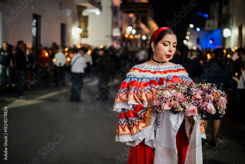 Mujer sahumadora vestida con traje típico tradicional participa en una procesión nocturna durante la Semana Santa en Popayán, Colombia. Sostiene un ramo de flores mientras esparce sahumerio 