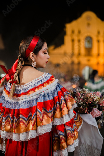 Mujer sahumadora vestida con traje típico tradicional participa en una procesión nocturna durante la Semana Santa en Popayán, Colombia. Sostiene un ramo de flores mientras esparce sahumerio 