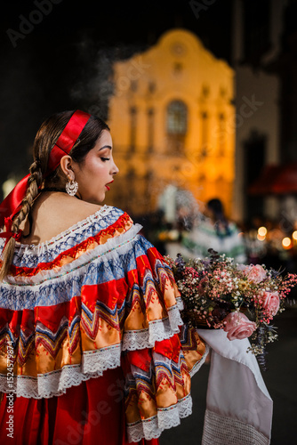 Mujer sahumadora vestida con traje típico tradicional participa en una procesión nocturna durante la Semana Santa en Popayán, Colombia. Sostiene un ramo de flores mientras esparce sahumerio 