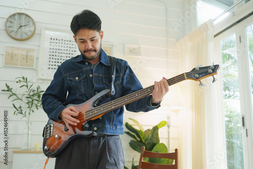 Asian musician man playing an electric bass guitar while standing in a well-lit room.