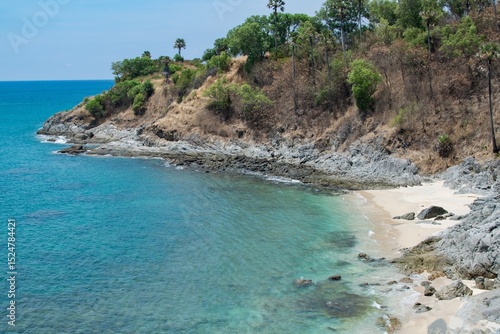 A small sea bay with blue water and white sand on the background of a cliff with palm trees