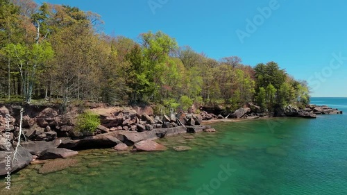 A breathtaking view of Madeline Island Lake Superior shoreline, with crystal-clear turquoise water, rocks, and vibrant spring trees, perfect for a scenic getaway