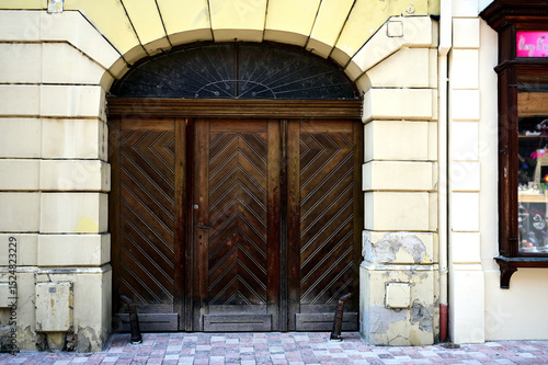 beautiful old arched brown wooden gate to residential home. vintage european street. stucco exterior elevation. stone road pavement. historic vintage building. travel and tourism concept