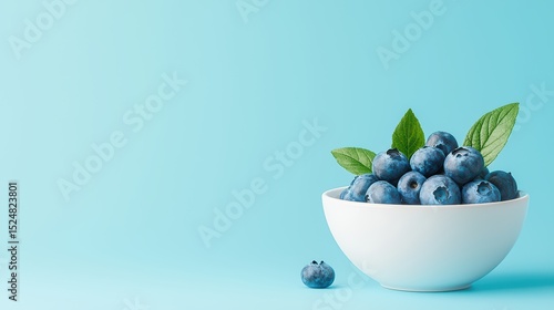 Fresh blueberries in white bowl with green leaves against soft blue background for healthy eating and nutrition concepts