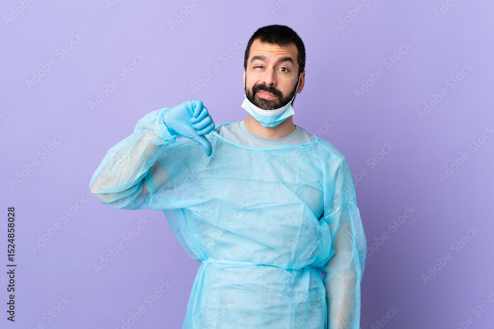 Surgeon man with beard with blue uniform over isolated purple background showing thumb down with negative expression Surgeon man with beard with blue uniform over isolated purple background showing thumb down with negative expression