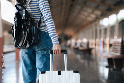 Stylish young woman traveling at train station with suitcase, traveling alone on vacation or business trip, enjoying summer city adventure.