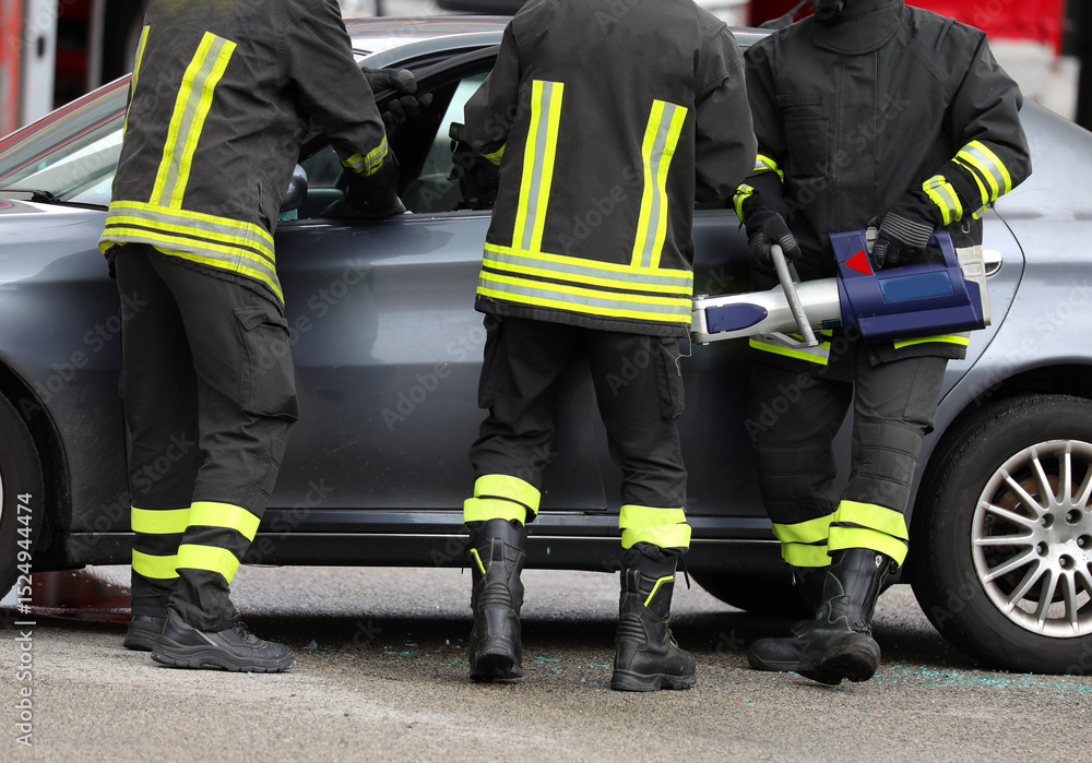 Obraz premium Three firefighters use a powerful hydraulic retractor called jaws OF LIFE to open car door after traffic accident