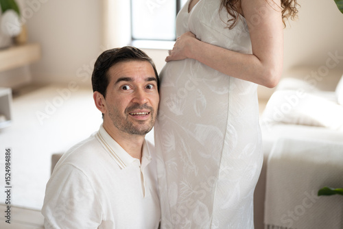 Future father listening to pregnant belly of his wife at home. Father's day concept