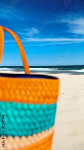 Close up of woven tote bag with leather handles on white sand beach against blue sky