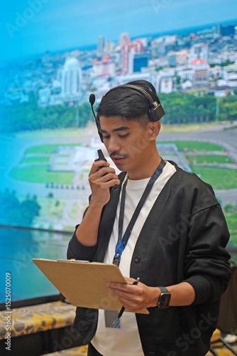 Asian male stage manager directs the show on stage using a headset, walkie-talkie, and clipboard, showing the professional work atmosphere behind the scenes of a show production.