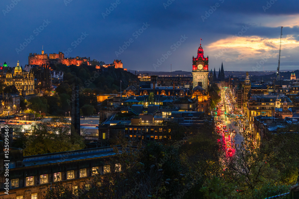 Obraz premium Nächtlicher Blick über Edinburgh mit dem beleuchteten Uhrturm des Balmoral Hotels und der Silhouette von Edinburgh Castle, städtische Abendstimmung über der historischen Hauptstadt Schottlands