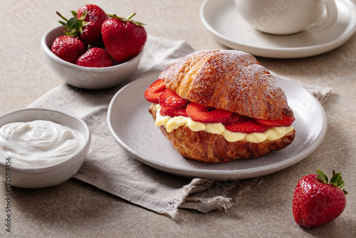 Croissant with strawberries and vanilla cream on plate with coffee and yogurt