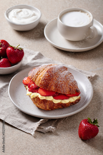 Croissant with strawberries and vanilla cream on plate with coffee and yogurt
