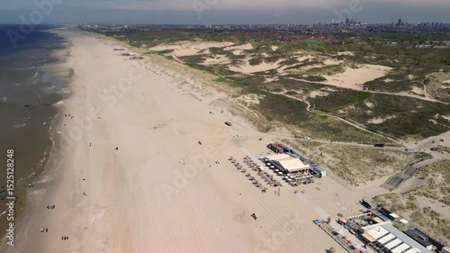 Wallpaper Mural A beautiful aerial view of a sandy beach with rows of beach huts, people relaxing by the shore, and gentle waves meeting the coast, bordered by grassy dunes in the foreground. Torontodigital.ca