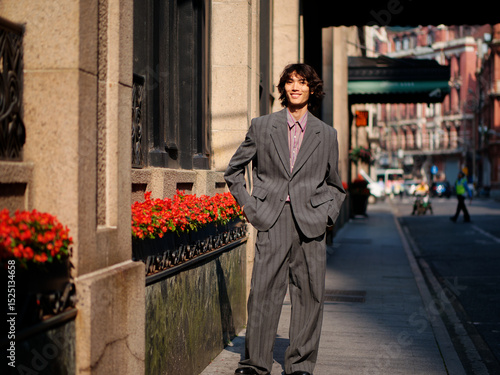 Portrait of handsome Chinese young man wearing gray suit smiling in the street, young guy with black curly hair with urban background. Male fashion, cool Asian young man lifestyle.