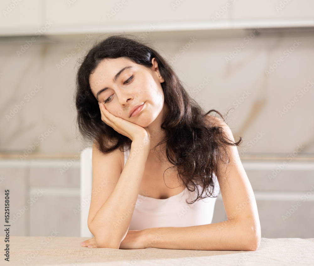 Portrait of a frustrated young woman sitting in a home kitchen Portrait of a frustrated young woman sitting in a home kitchen