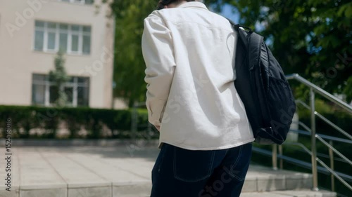 Teen schoolboy with backpack walking to school entrance early in the day