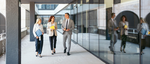 Business team walking and discussing work in office corridor. Modern copyspace.