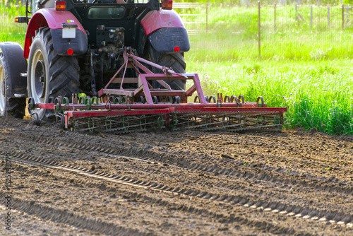 Quadro em tela Tractor tilling soil in sunny field with greenery and freshly plowed earth